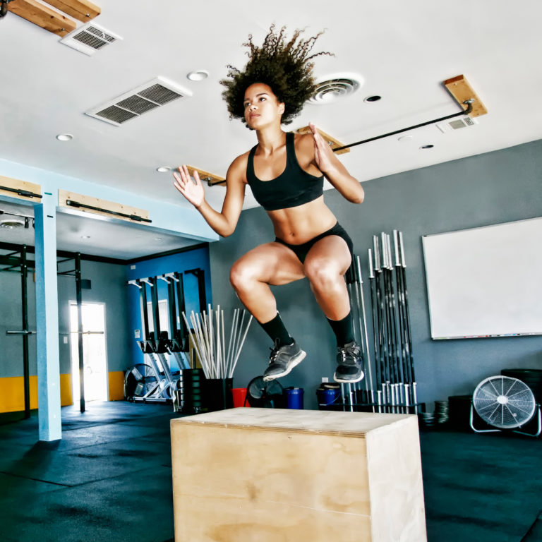 Female athlete performing plyometric jump over box