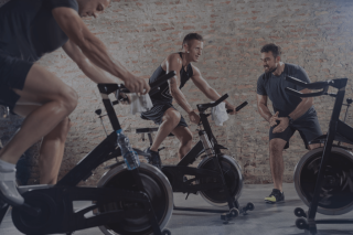 Group of men coached on exercise bikes by personal trainer