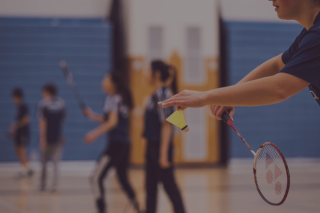 Person awaiting badminton serve in school gym